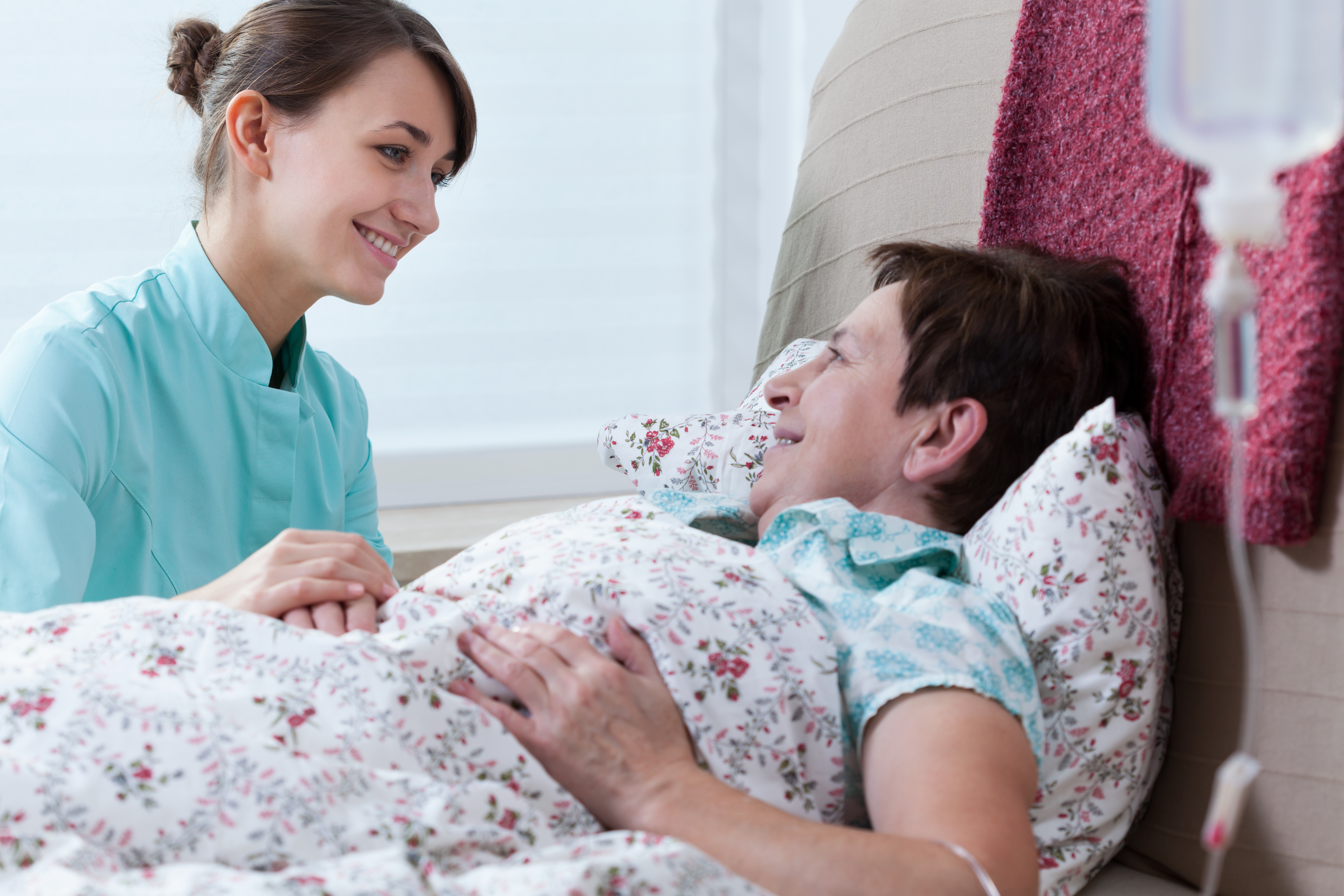 Ill woman lying in bed and her helpful nurse